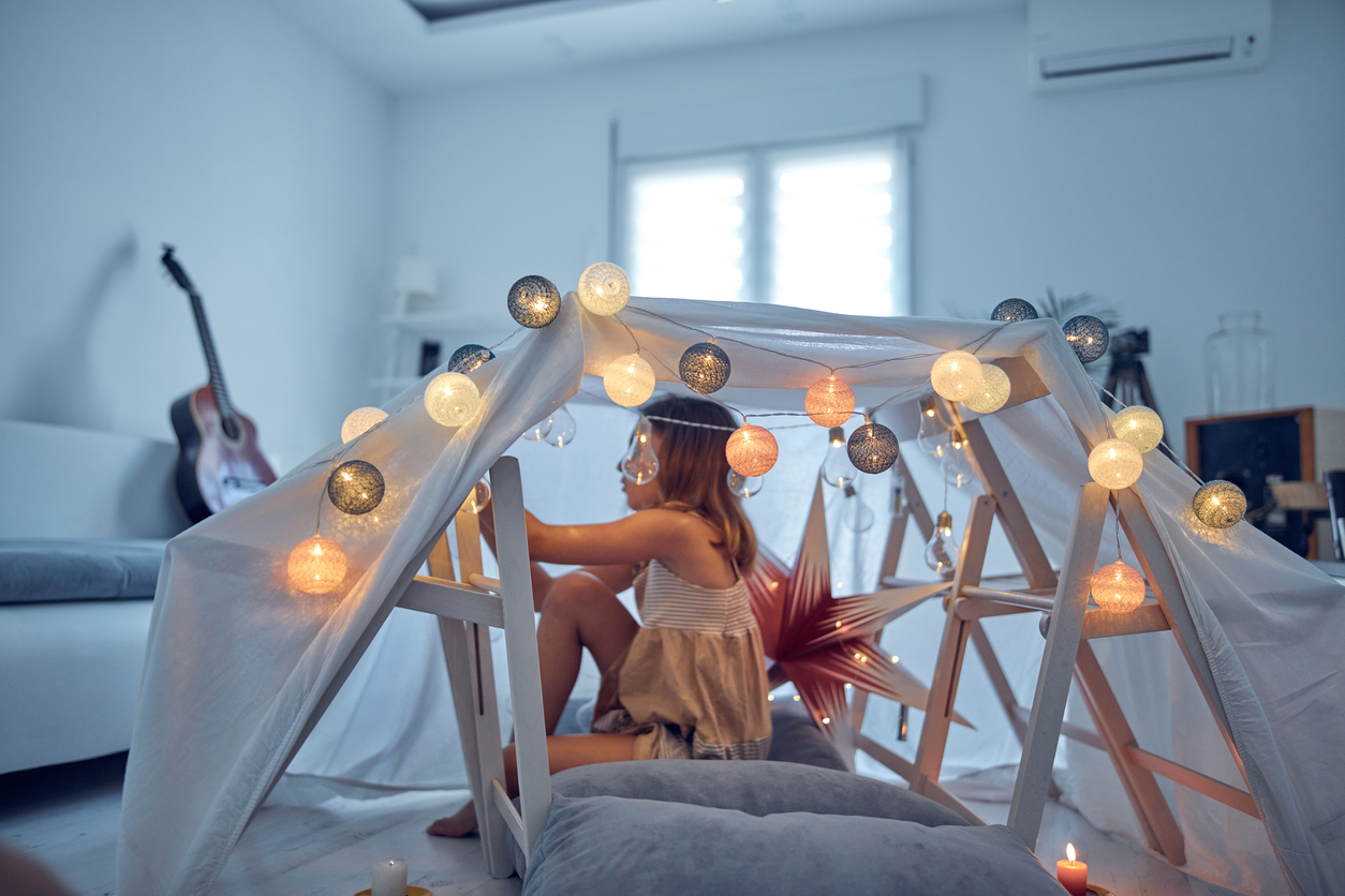 Little girl playing and making a house tent in the room.